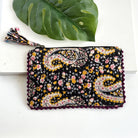 A black floral-patterned rectangular pouch against a white background with a large leaf in the background.