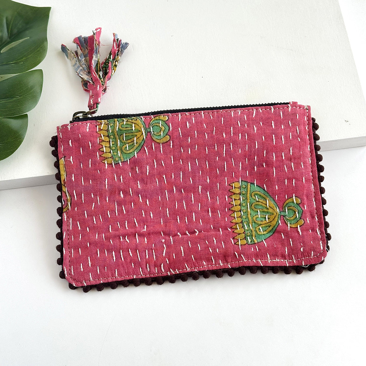 A pink rectangular pouch against a white background with a large leaf in the background.