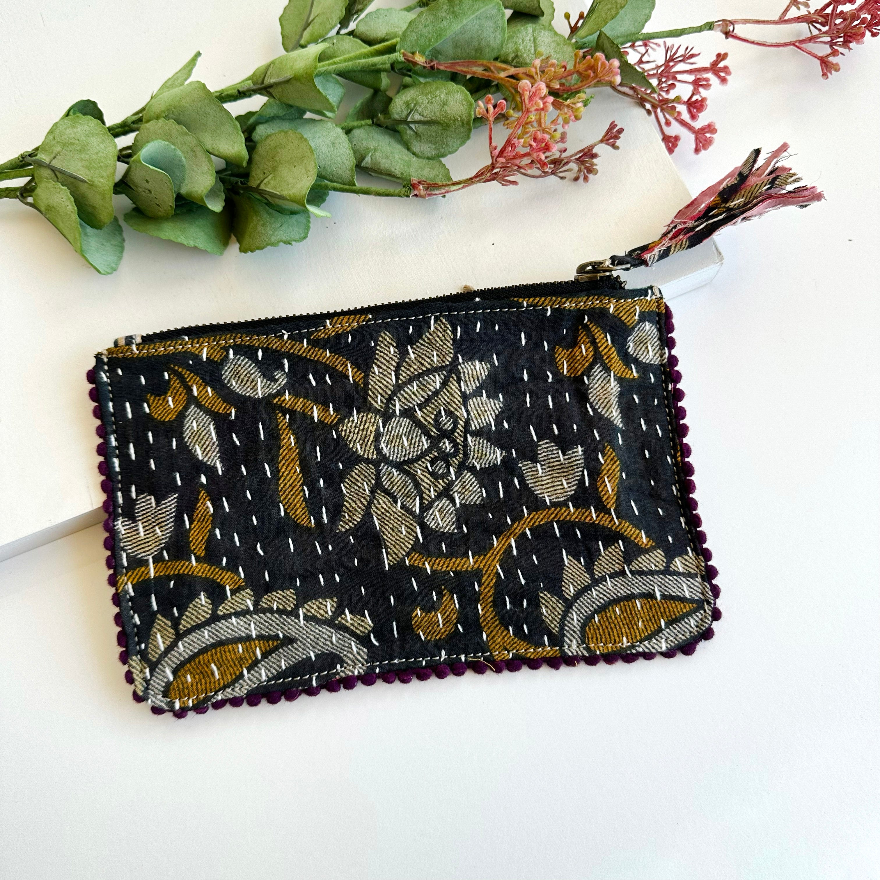 A black and gold rectangular pouch against a white background with floral elements along the top.