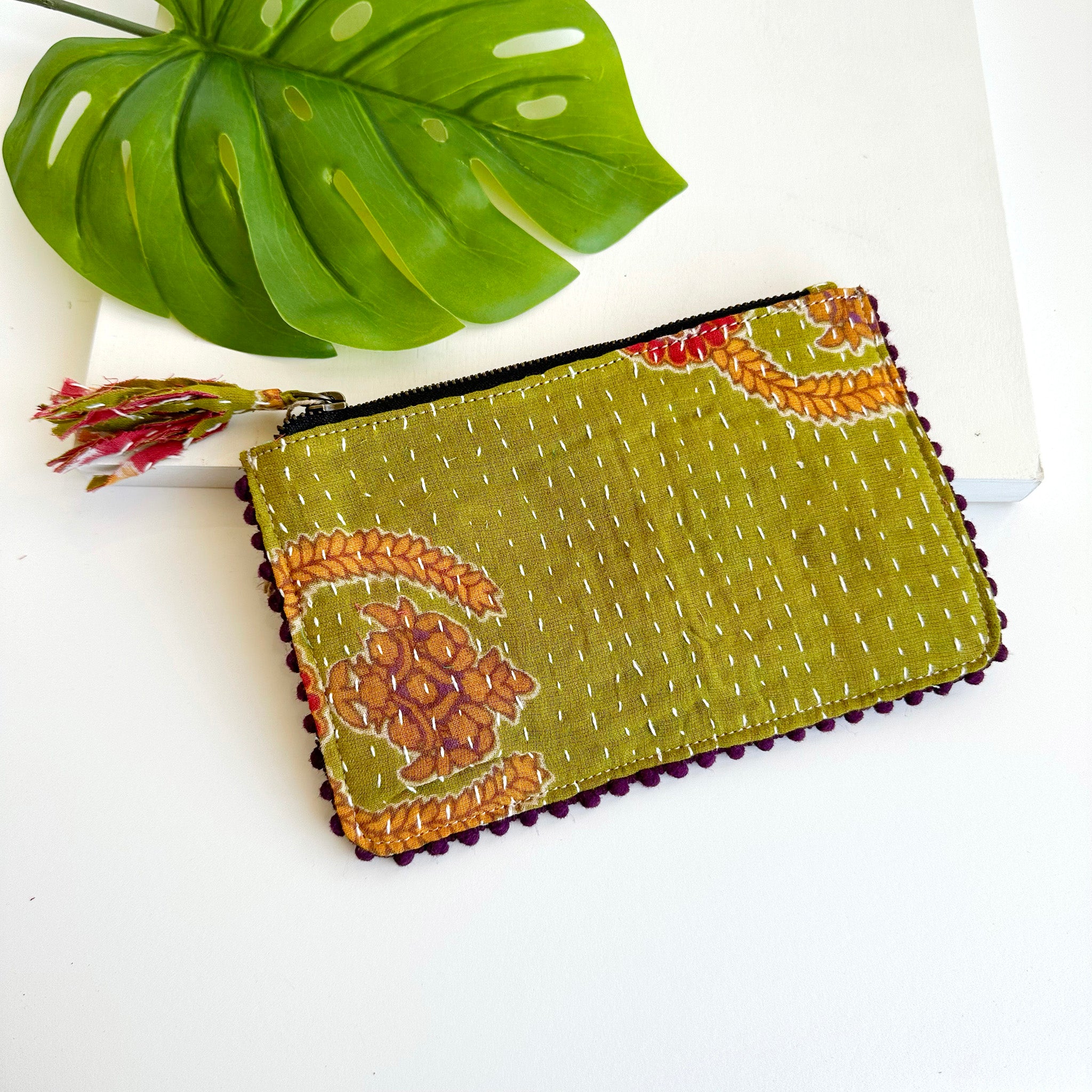 A green rectangular pouch against a white background with a large leaf in the background.