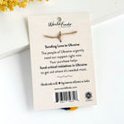 The back of a carded item leaning against a white background with a yellow flower to the left.