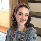 A woman in a denim shirt and multicolor jewelry & accessories smiles.