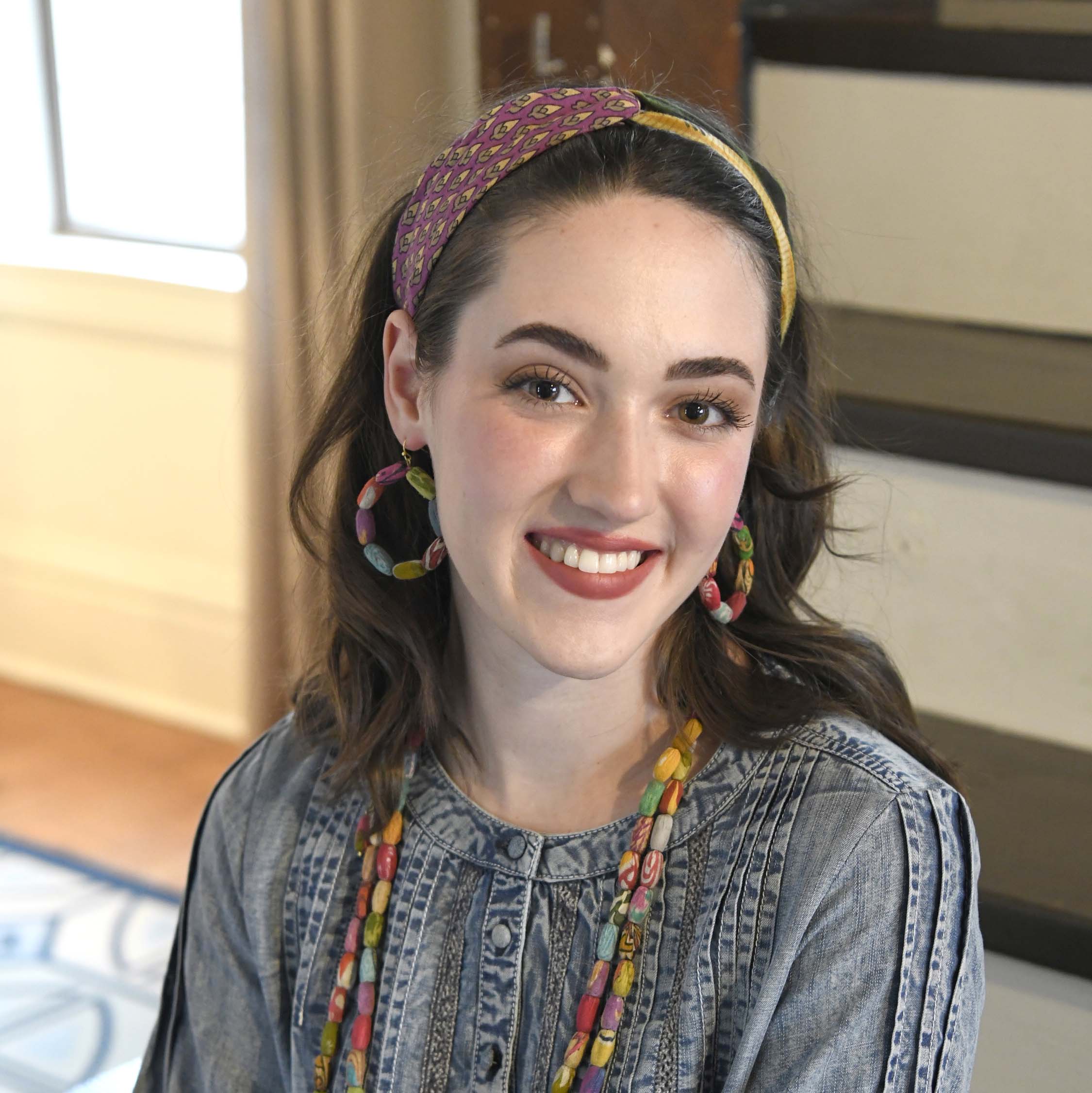 A woman in a denim shirt and multicolor jewelry & accessories smiles.