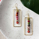 A pair of gold and multicolor, beaded earrings on a white background.