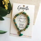 A green beaded bracelet tied to a card that reads "Growth" against a white background with a green leaf to the left.