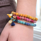 A close up of a woman's wrist and the yellow, pink and blue beaded bracelets she is wearing.