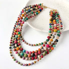 A five-strand multicolor necklace hangs off a white plate on a white surface.