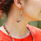 A close up of a woman's ear and the multicolor beaded earring she is wearing.