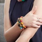 A woman's hand rests on her arm while displaying her stack of three colorful beaded bracelets.