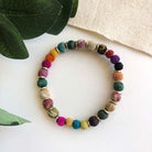 A multicolored beaded bracelet against a white background with green leaves in the top corner.