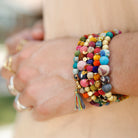 A close up of a woman's wrist and the five beaded multicolor bracelets she is wearing.