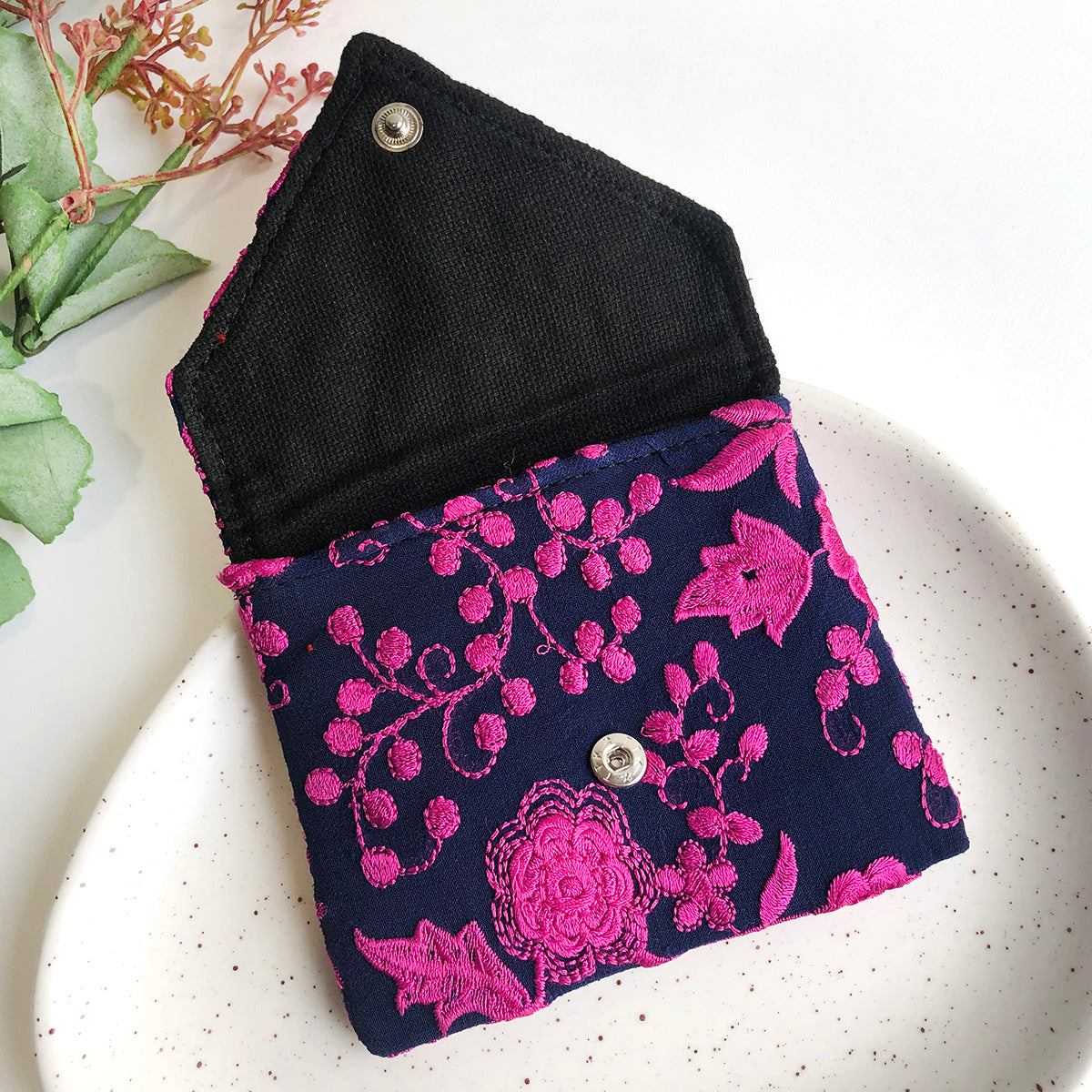 A blue and pink embroidered pouch is open to reveal a black cotton lining.