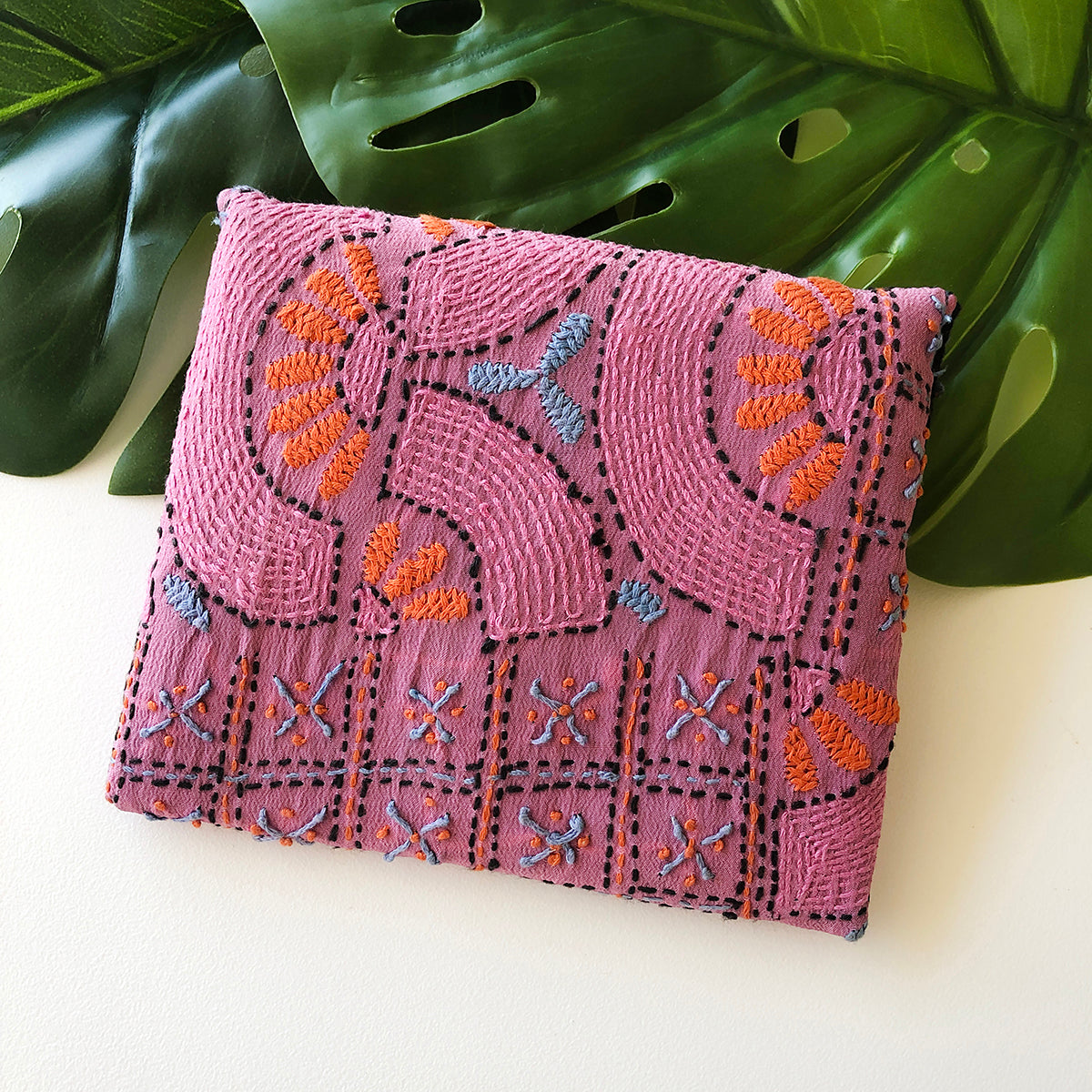 A close up of a pink envelope-style pouch highlights the traditional embroidery.