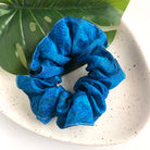 A large blue scrunchie rests on a white speckled plate with a green leaf.