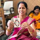 A woman in a pink Sari holds up a carded bracelet that reads "Unity" and she smiles.